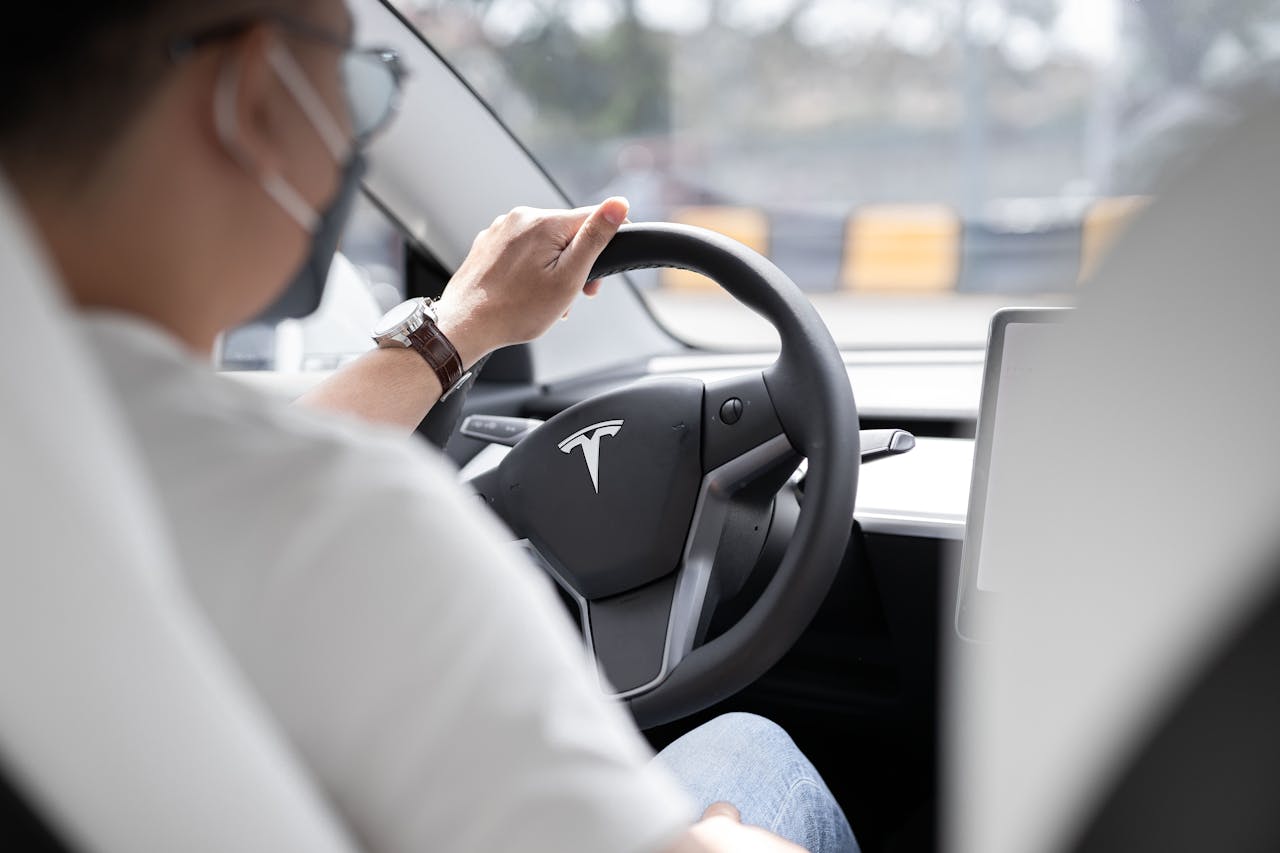 Close-up photo of a person driving a Tesla, showcasing modern vehicle interior design.
