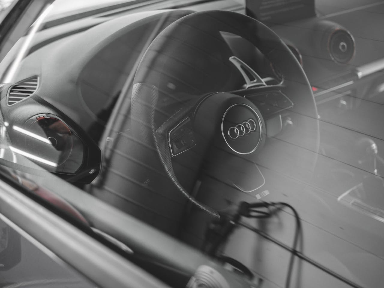 Photo of Audi car interior through the window focusing on the steering wheel and dashboard.